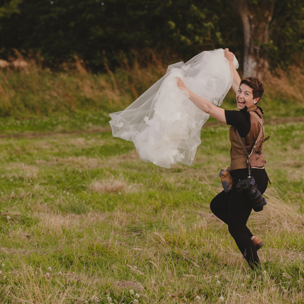 Aberdeen wedding photographer lending a hand to her bride by carrying her veil and running through the fields with it.