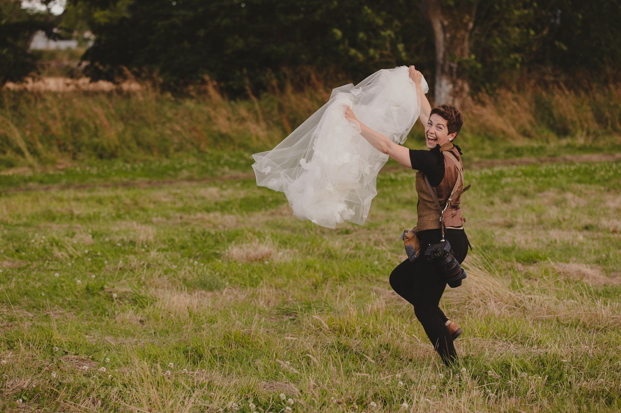 Aberdeen wedding photographer lending a hand to her bride by carrying her veil and running through the fields with it.