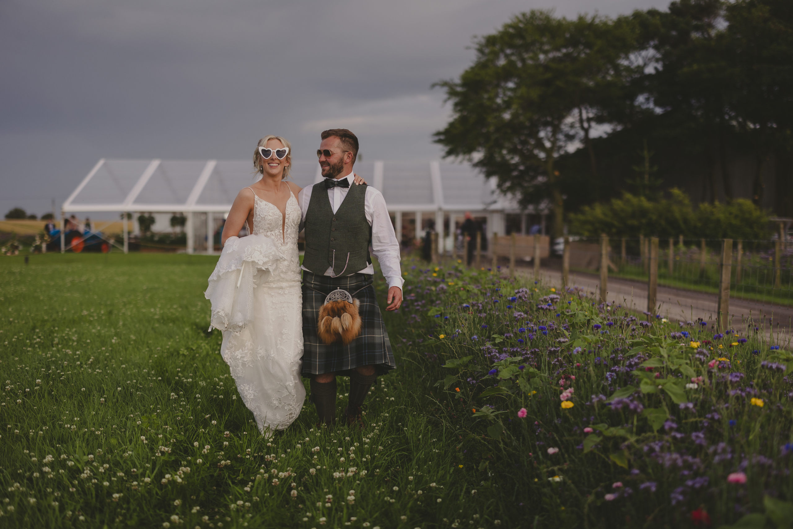 Bride and groom walking together through field wearing sunglasses